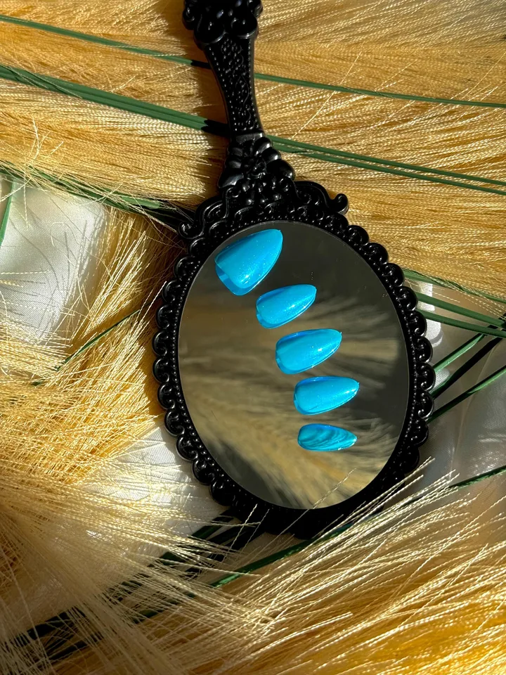 Five bright turquoise blue almond press on nails with a glossy pearlescent finish, displayed on a black ornate mirror.