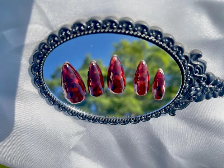 Five glossy almond press on nails with a translucent reddish brown and dark tortoiseshell pattern on an ornate mirror.