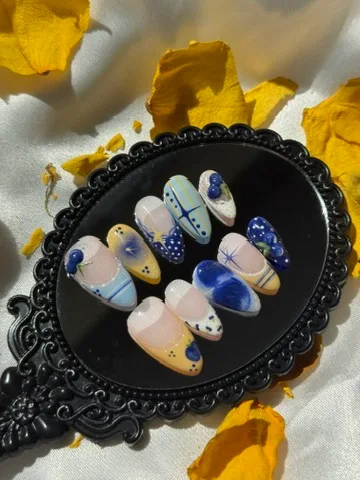 Blueberry Picnic press-on nails with blue and yellow French tips, plaid, blueberry accents and sparkles on a black mirror.