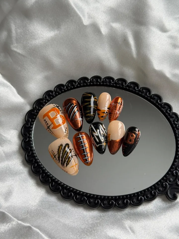 Orange, black and white Cincinnati nail art with tiger stripes, football details and a B design on a black oval mirror