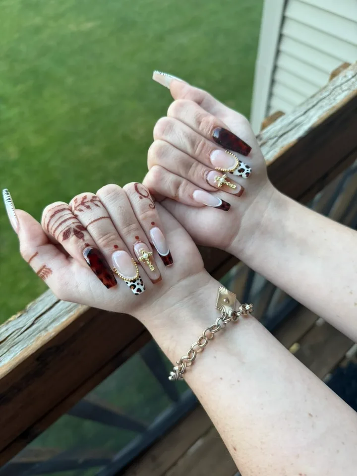 Hands wearing tortoiseshell and nude coffin nails with animal-print tips, gold beading and gold charms