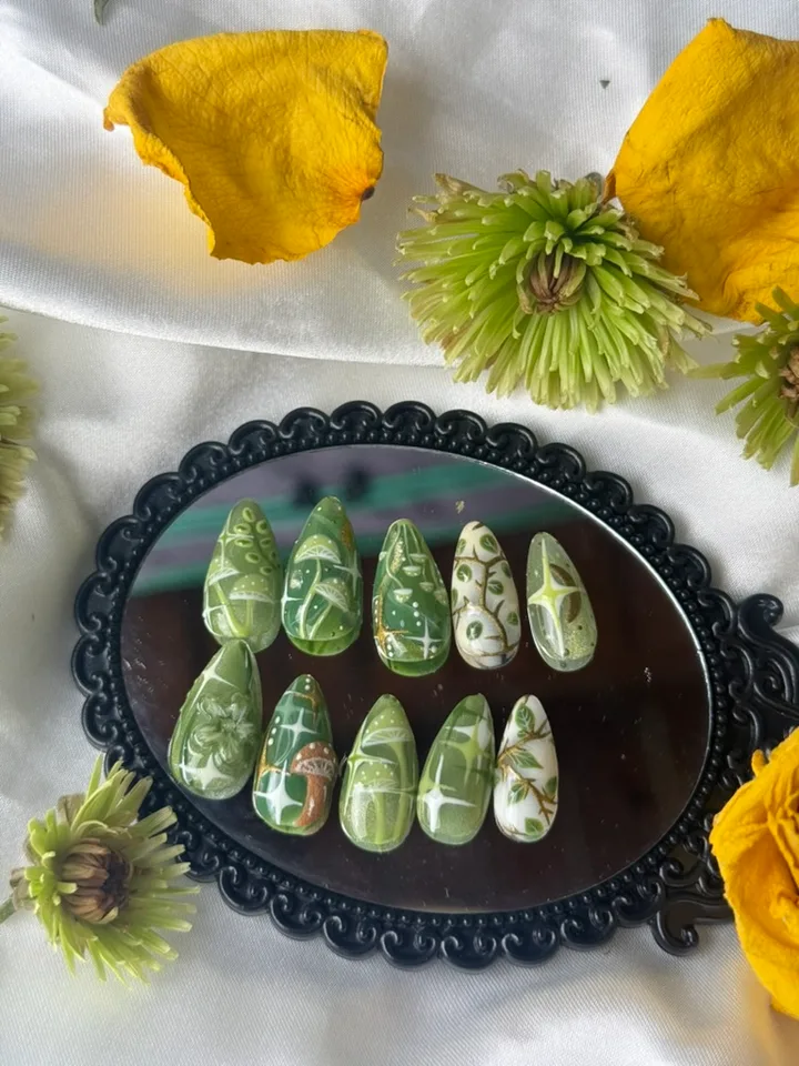 Green woodland nail art with mushrooms, leafy vines, white starbursts, gold accents and a sculpted flower on a black mirror